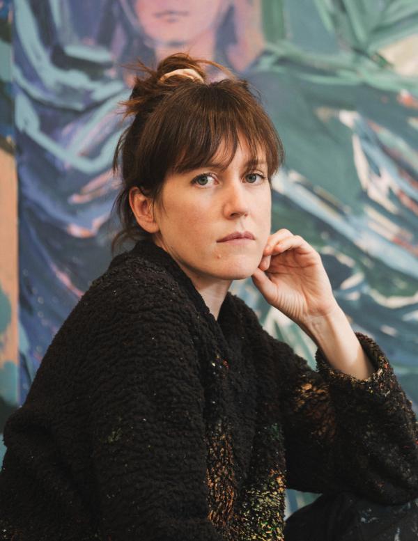 Claire Tabouret assise devant une de ses oeuvres 