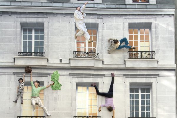 Un bâtiment de type haussmannien avec plusieurs personnes qui s'y accrochent (mise en scène)